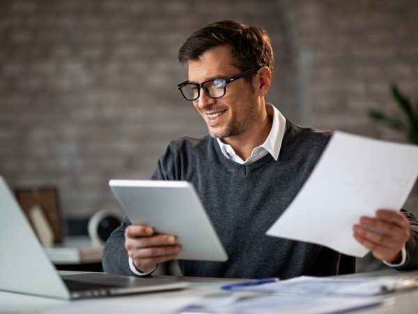 Happy businessman using touchpad and laptop while working on business reports in the office.