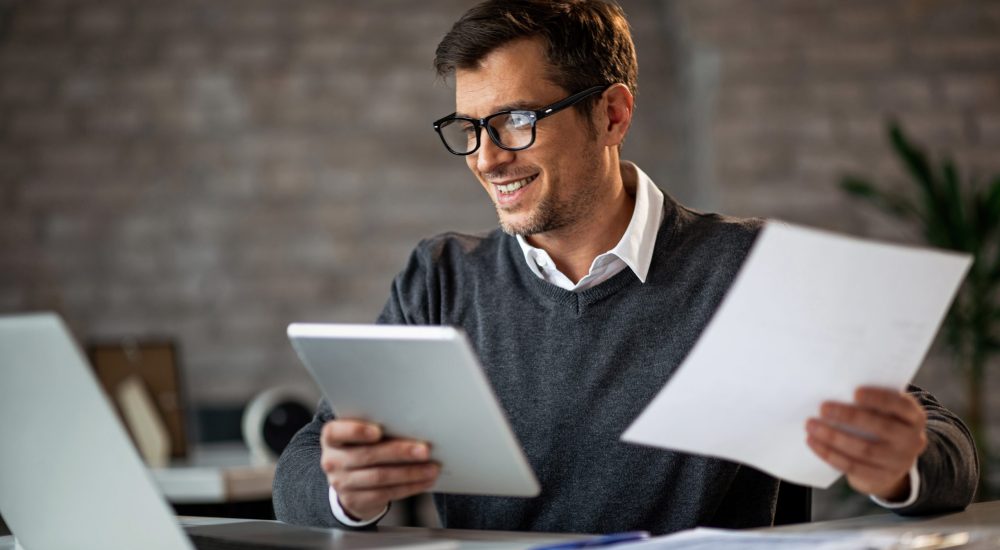 Happy businessman using touchpad and laptop while working on business reports in the office.